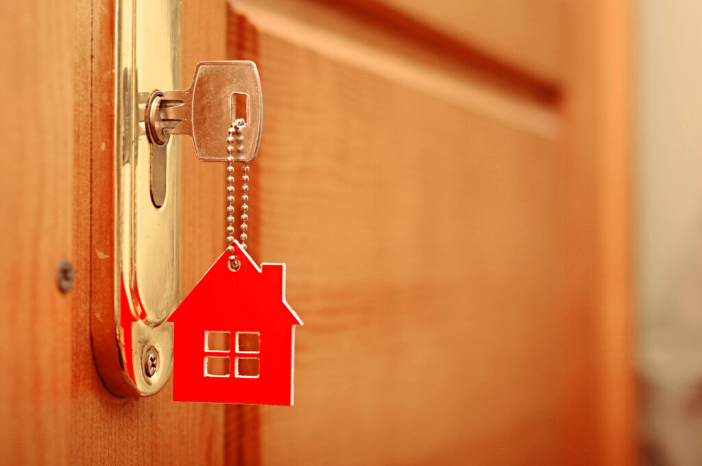 a gold key inserted into a lock of a home with a red home on the keychain